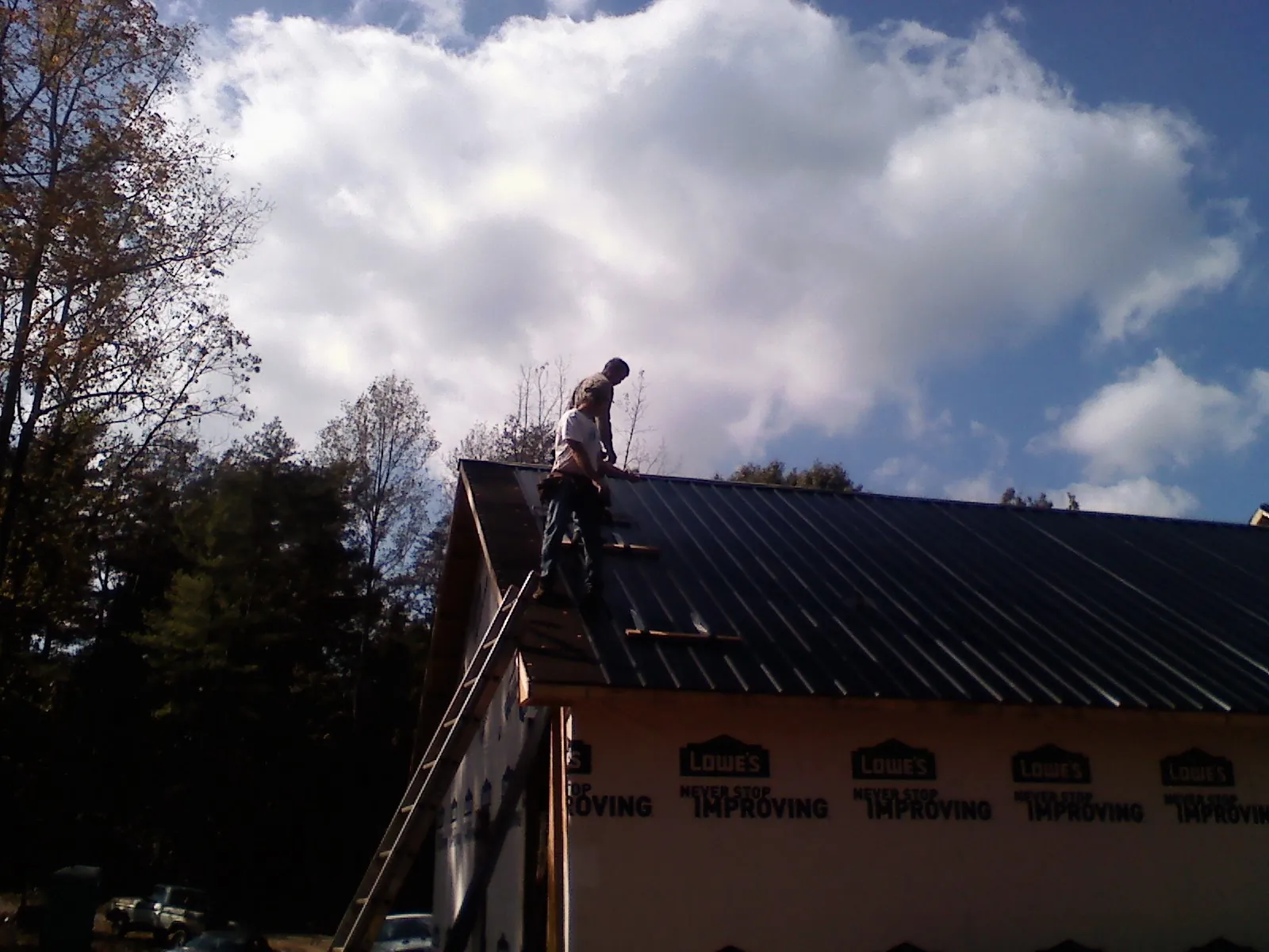 Roofer fastening dark metal panels high against a cloudy sky, from a Roof Inspection job in Ragland