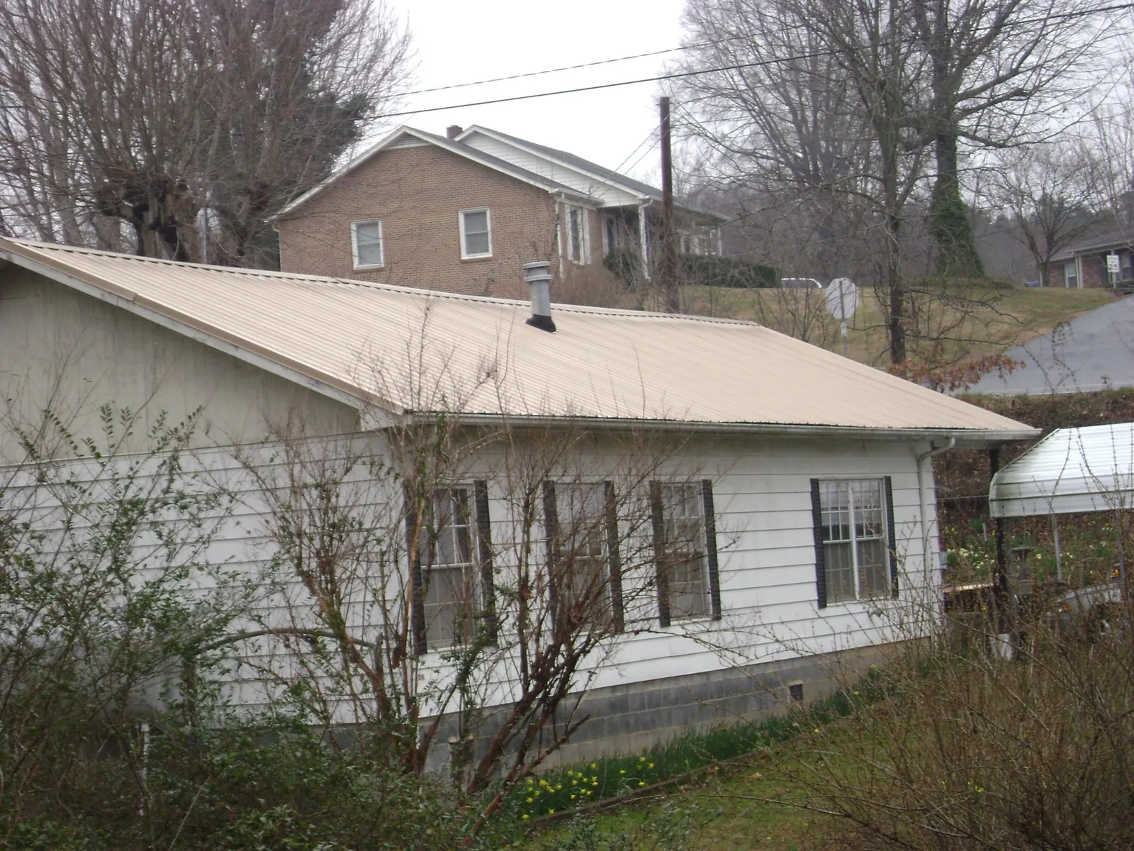 Tan metal roof on a white sided house set into a hillside — Commercial Roofing by Roofing Brothers in Ragland